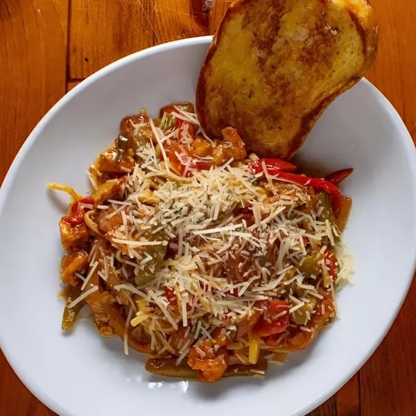 Cajun pasta with chicken, peppers, and onions, topped with parmesan cheese and a side of garlic bread.