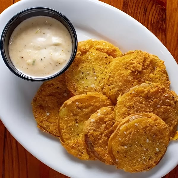 Golden-brown fried green tomatoes with a side of creamy dipping sauce on a white plate.