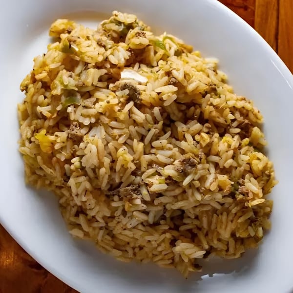 A white oval plate filled with a generous serving of Boudreaux's II Cajun dirty rice.